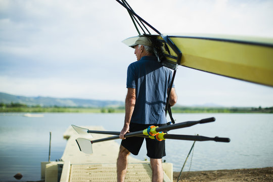 A middle-aged man carrying oars and a rowing shell on his shoulder. 