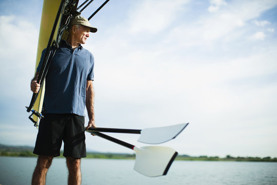 A middle-aged man carrying oars and a rowing shell on his shoulder. 