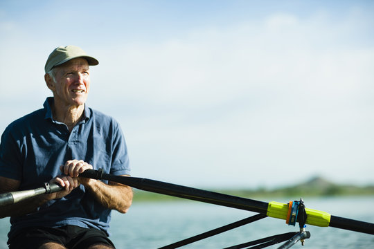 A middle-aged man rowing a single scull rowing boat on the water. 