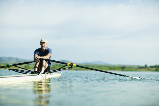 A middle-aged man rowing a single scull rowing boat on the water. 