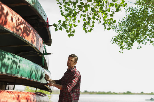 A man stacking narrow rowing boats and lashing them onto a trailer or stand. 