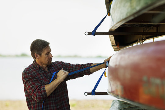 A man stacking narrow rowing boats and lashing them onto a trailer or stand. 