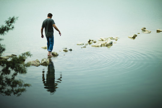 Man walking barefoot on stepping stones in lake