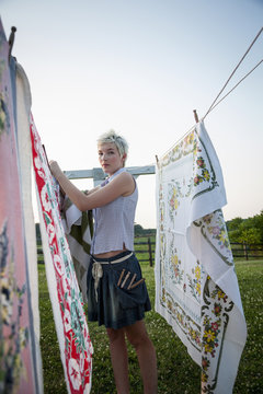 A young girl, teenager, hanging out the washing, pegging patterns fabric sheets to a washing line. 