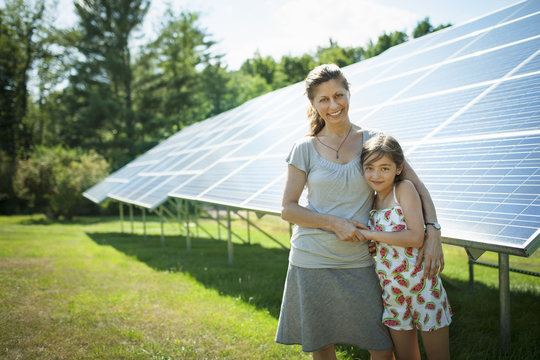 A Child And Her Mother In The Fresh Open Air, Beside Solar Panels On A Sunny Day At A Farm In New York State, USA.