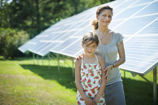 A child and her mother in the fresh open air, beside solar panels on a sunny day at a farm in New York State, USA.