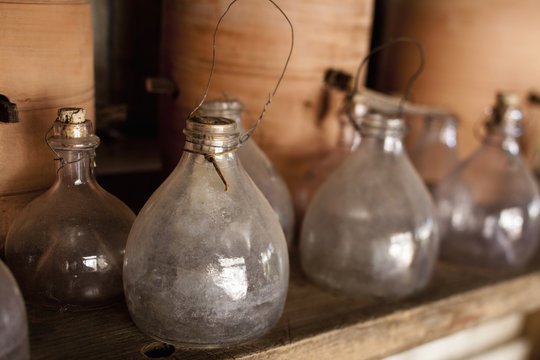 A row of glass jars, with stoppers and large clay pots on a shelf. 