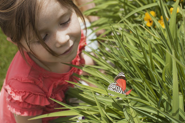 A young girl looking at a colourful butterfly in the grass. 