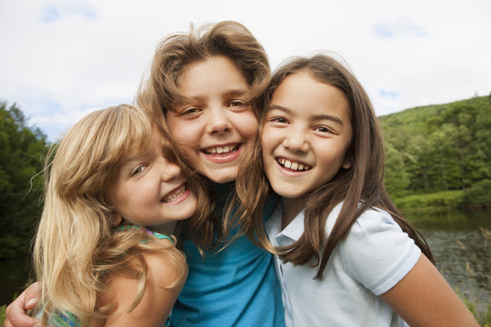Three young girls, friends side by side, posing for a photograph in the open air.
