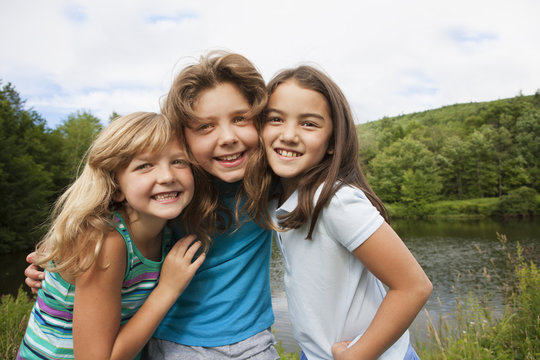 Three young girls, friends side by side, posing for a photograph in the open air.