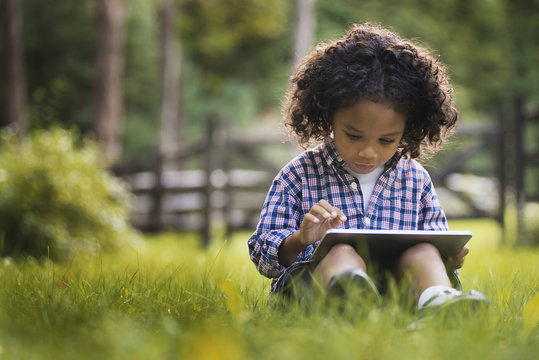 A small boy sitting on the grass using a tablet computer.