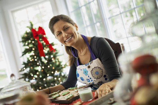 A woman working on organic homemade Christmas cookies, decorating and sprinkling decorations on green icing. 