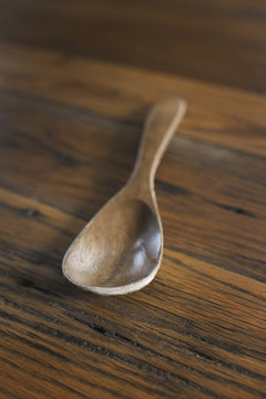 A smooth polished wooden ladle or spoon on a  grained wooden tabletop.