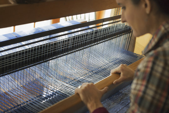 A woman seated at a wooden handloom creating a handwoven woollen fabric, with a blue and white pattern.