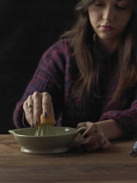 A woman holding a cut orange half, and using an orange squeezer to extract the juice, on a wooden table.