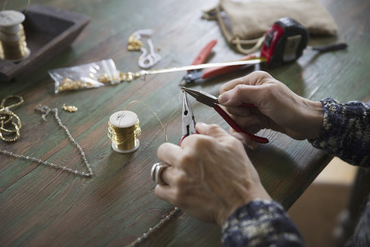 A tabletop with jewellery making equipment. Hands twisting wire on a necklace.