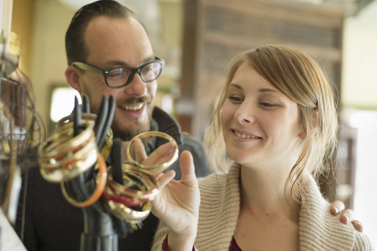 Two people, a man and woman looking at the objects displayed on a mannequin hand, antique jewellery and objects.