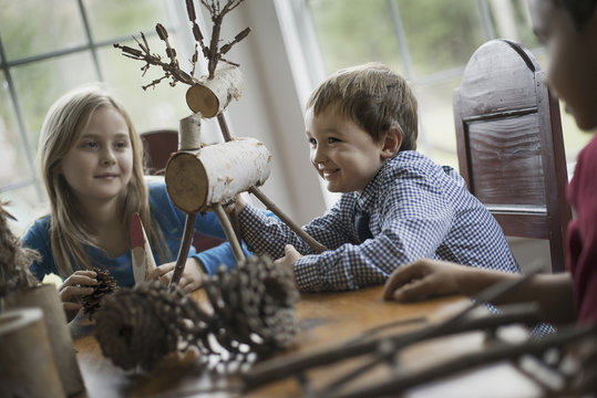 Three children sitting at a table in family home. A twig reindeer in the centre, with branches and twigs to make objects.