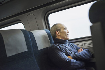 A mature man sitting in a window seat on a train journey, looking out into the distance.