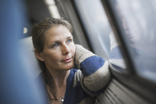 A woman sitting at a window seat in a train carriage, resting her head on her hand. Looking into the distance.