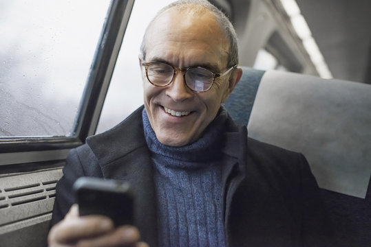 A mature man sitting by a window in a train carriage, using his mobile phone, keeping in touch on the move.