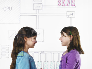 Two children facing each other behind a drawing of a computer motherboard circuit drawn on a see through clear surface.