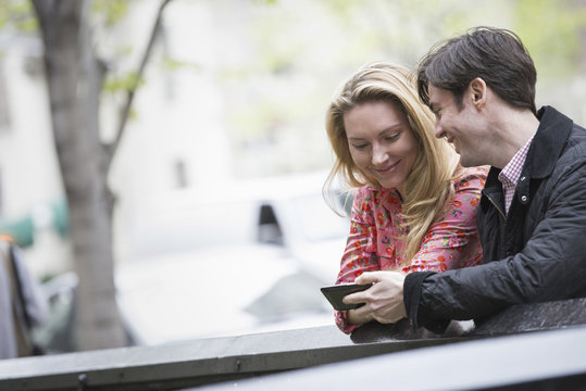 City life in spring. Young people outdoors in a city park. Two people sitting side by side, looking down at a smart phone.