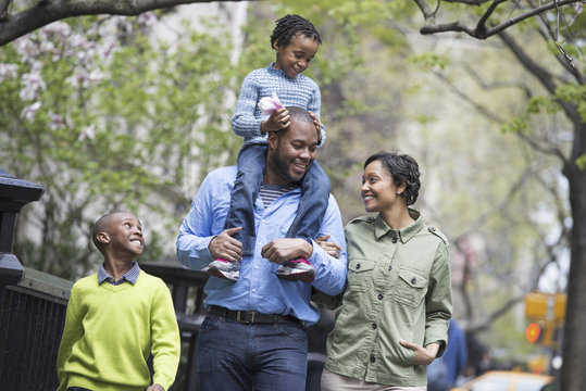 A New York city park in the spring. A family, parents and two boys.  A child riding on his father's shoulders.