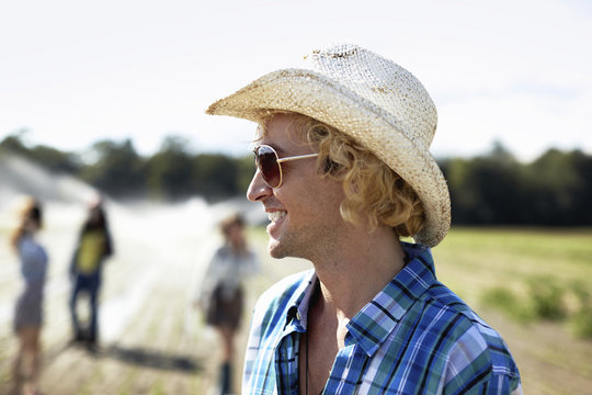 A young man in straw hat and sunglasses. Irrigation sprinklers in the field.