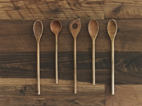 Home cooking. A wooden table with a varied wood grain and colour. Five wooden spoons in a row. 