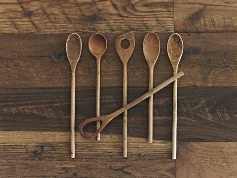 An arrangement of six wooden spoons of a variety of shapes and sizes on a wooden table. 