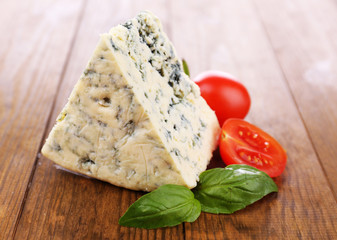 Tasty blue cheese with basil and tomato, on wooden table