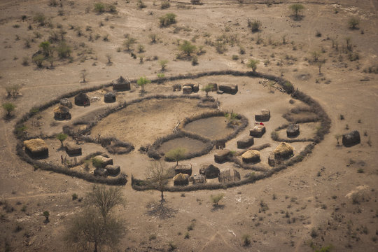 An aerial view of a small rural village settlement, with traditional buildings and animal enclosures. 