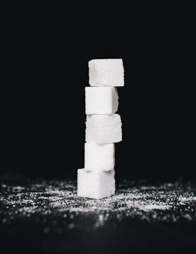 Stack of sugar cubes, balancing one on top the other, on black backdrop