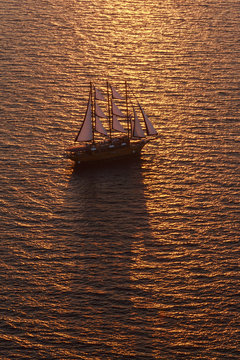 A three-masted sailing ship with full sail on the Aegean Sea at sunset.
