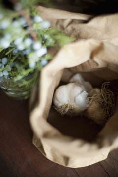 Organic ingredients on a table. Garlic bulbs in a brown paper bag. A herb with  blue flowers. Fresh ingredients.