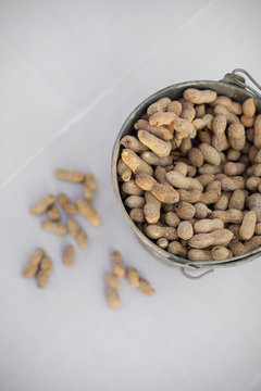 A metal container with a handle. Peanuts with their husks on. Organic nuts, Arachis hypogaea. Shells on.
