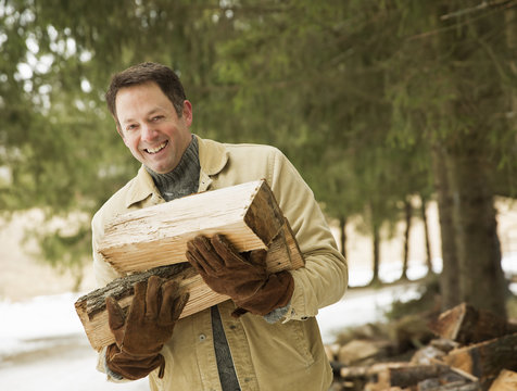 A man outdoors carrying an armful of logs