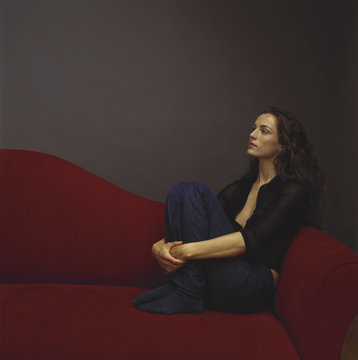 A woman dressed in black seated on a red couch.