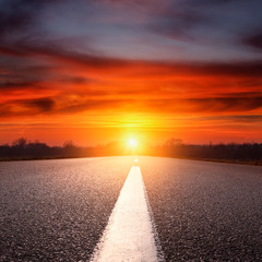 Driving on an empty asphalt highway towards the setting sun