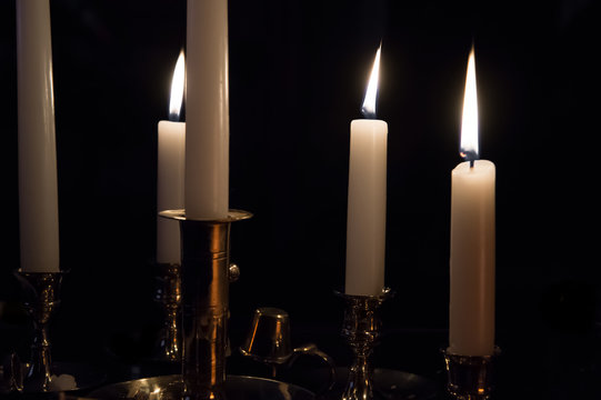 Multiple white burning candles in brass holders