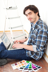 Young man using laptop while choosing color of his flat