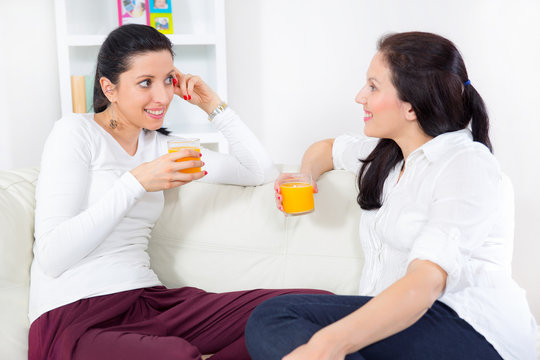Two happy young female friends with juice conversing