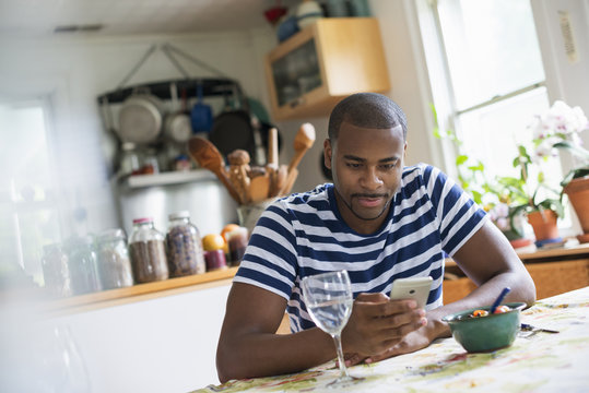 A man sitting at a table using a smart phone. Fruit dessert and a glass of wine at hand.