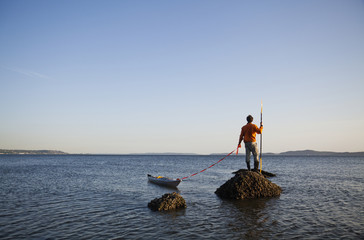 A sea kayaker stands on a rock in the water at sunset off the coast of Seattle in the Puget Sound, Washington, USA.