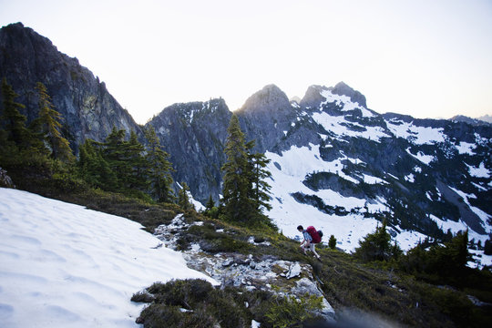 A young man hikes around a snow patch while going to the summit of a large mountain in the Cascades of Washington, USA.