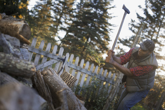 A man wielding an axe, and chopping wood, splitting logs for the fire.