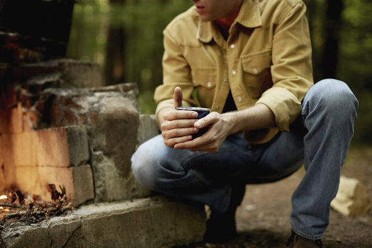 A man kneeling by a blazing camp fire.