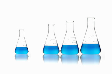 Conical glass scientific flasks holding blue liquids. Lined up in size order, with one set apart.
