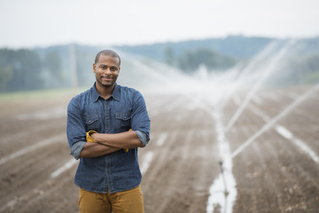 An organic vegetable farm, with water sprinklers irrigating the fields. A man in working clothes.